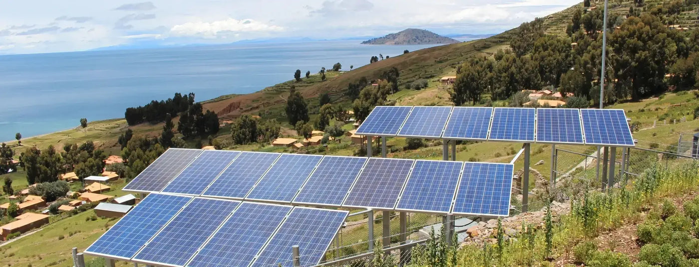 On the hillside overlooking a large expanse of water, multiple sets of solar panels are installed.