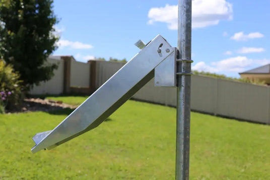 Close-up of a galvanized steel bracket designed for pole-mounting a solar panel, attached to a metal post in a grassy backyard.