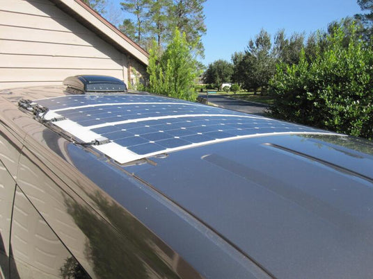 An array of flexible solar panels on a van roof, showing the black wiring neatly secured with cable mounts along the edge.