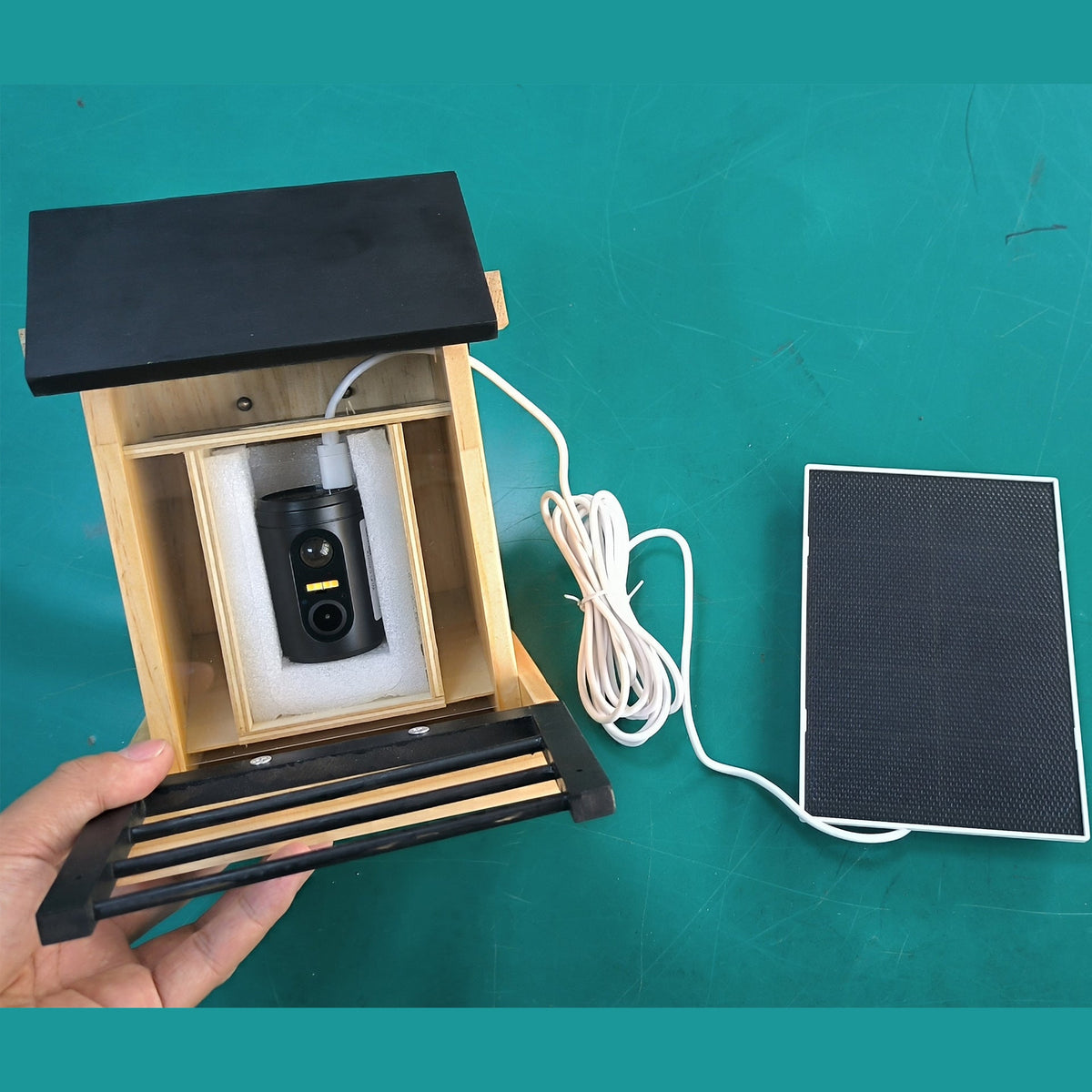 Wooden camera feeder and separate solar panel with connecting cable on a work surface