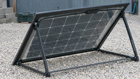 A single portable bifacial panel on an open rear stand is deployed over a pale gravel surface, with space behind the panel for reflected light.