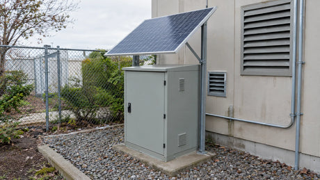 One compact finished PV panel staged above a constrained outdoor equipment enclosure with nearby vents and clearances visible, no permanent mounting or output claim.