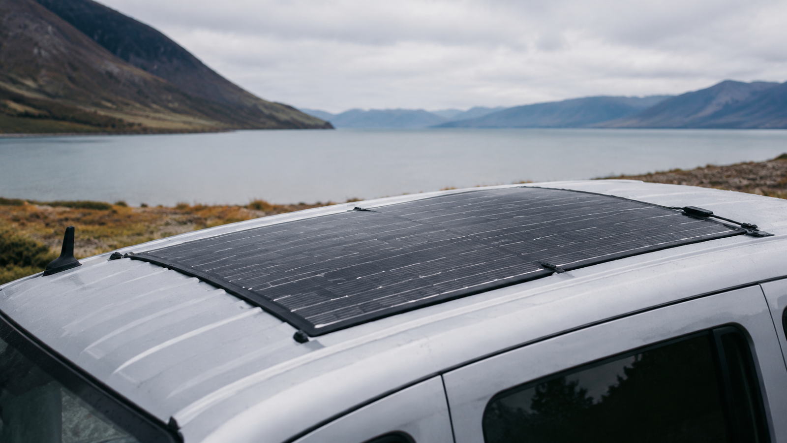 Thin flexible solar panel mounted across a curved vehicle roof in an outdoor setting