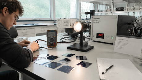 University laboratory setting with solar cell testing station, multimeter, light source, and silicon wafers on lab bench