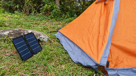 AI-retouched user photograph: Two-section folding solar charger laid beside an orange camping tent