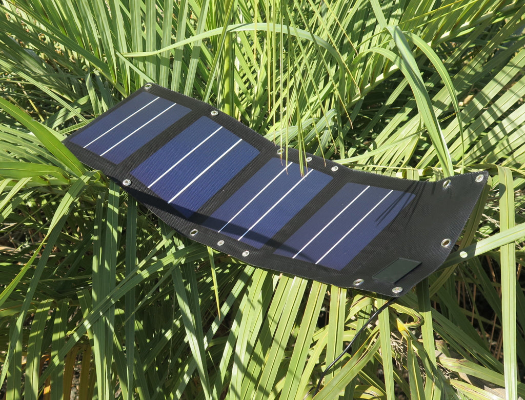 Portable flexible solar charger panel resting on green plants outdoors