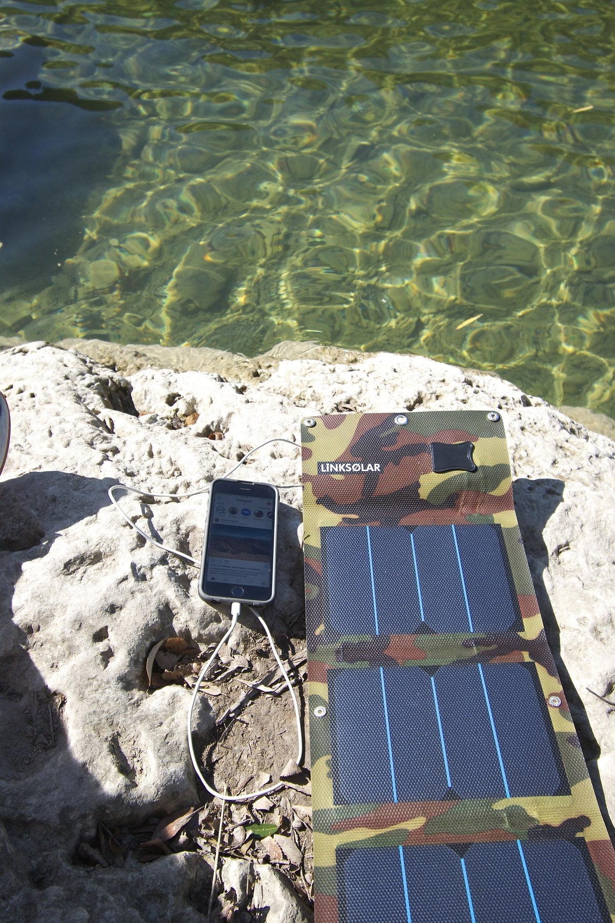 Portable solar charger charging a smartphone outdoors by a river