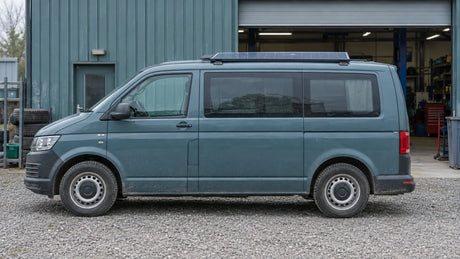 An unbranded camper van with a roof solar module is parked at a practical service site, illustrating an upgrade project with existing equipment retained.