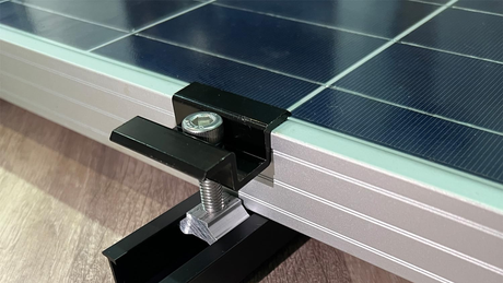Close-up of a black aluminum short solar rail, sliding nut, end clamp, and stainless fastener securing an unbranded framed panel.
