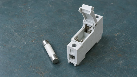 An unmarked cylindrical ceramic fuse link and separate empty modular holder rest on an inspection bench, illustrating a purchase that must identify both parts.
