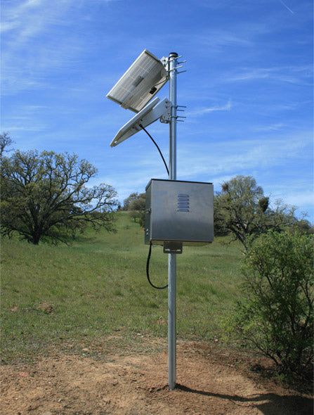 Small solar panel on a steel pole above a weatherproof equipment box in open grassland, the layout a shore-side battery and air pump enclosure follows