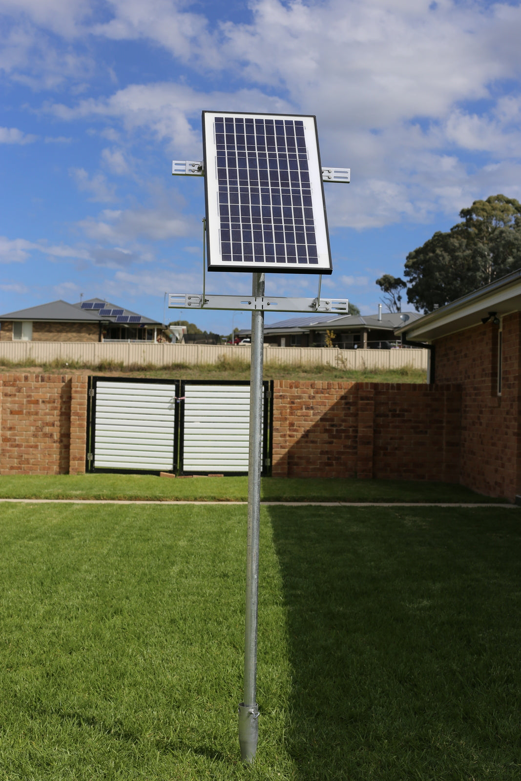 Small rigid solar panel on a galvanized pole in a backyard, the kind of mount used for a shed or coop fan