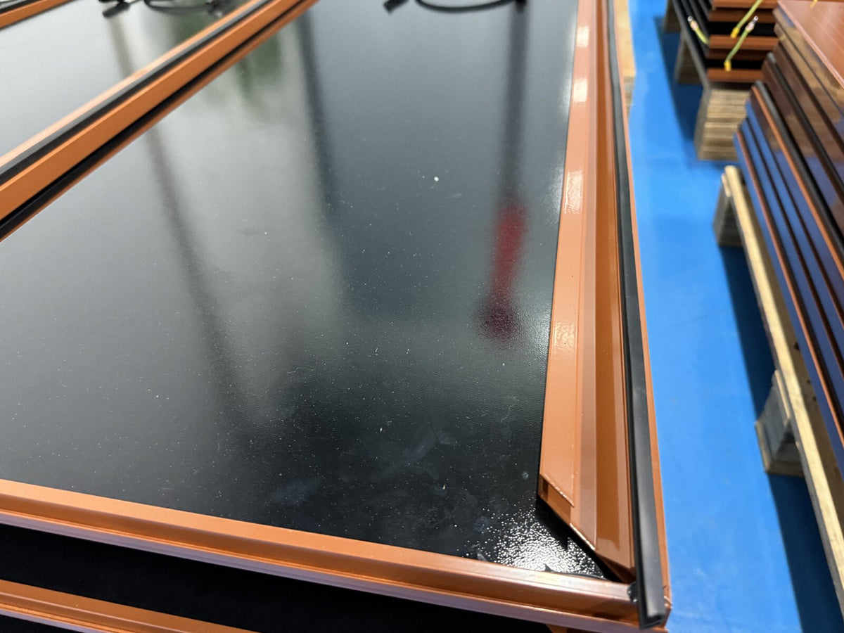 Finished black solar roof tiles with brown frames stacked on a warehouse floor
