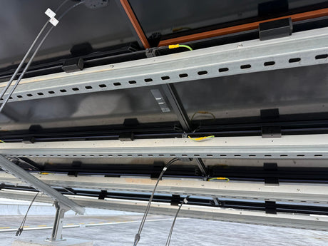 Underside view of a solar roof tile mounting rail with clips and wiring during installation