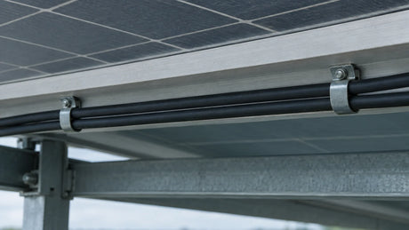 Insulated solar cables are held alongside a module-frame edge by small structural clips, illustrating cable positioning without a strain-relief or grounding claim.