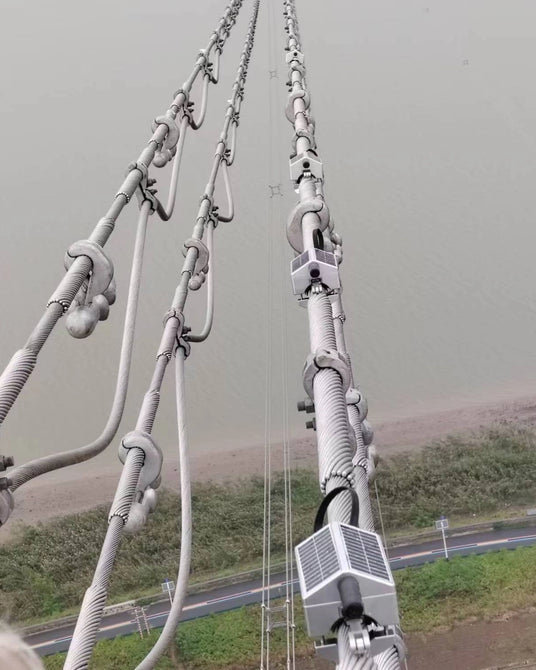 several solar-powered monitoring boxes and clamps installed along their length, overlooking a riverbank.