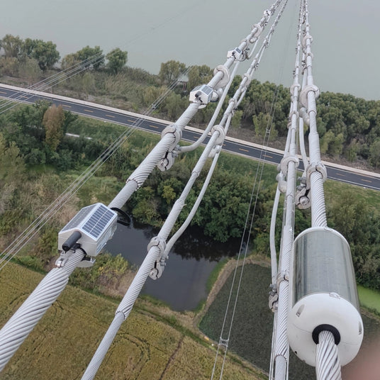 Looking down from the transmission tower, you can see multiple power lines and monitoring devices attached to the cables.