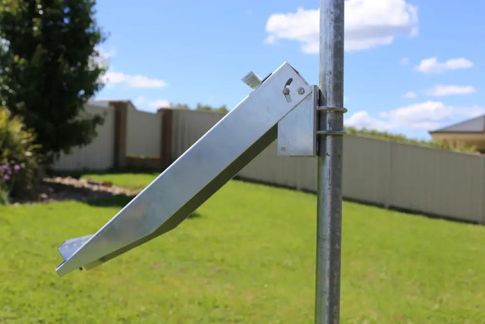 Close-up of a galvanized steel bracket designed for pole-mounting a solar panel, attached to a metal post in a grassy backyard.