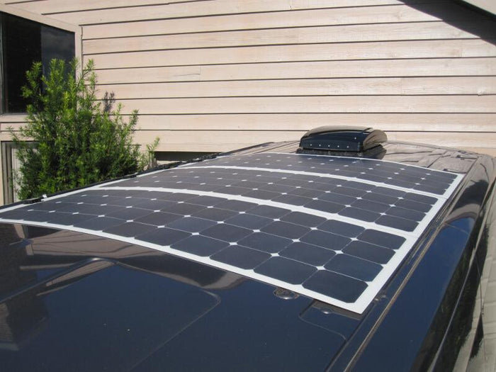 A clean installation of three flexible solar panels mounted flush on the dark gray roof of a van, with a black roof vent visible behind them.