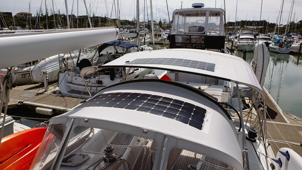 Two flexible solar panels mounted on the white canvas cover (bimini/dodger) of a sailboat in a busy marina.