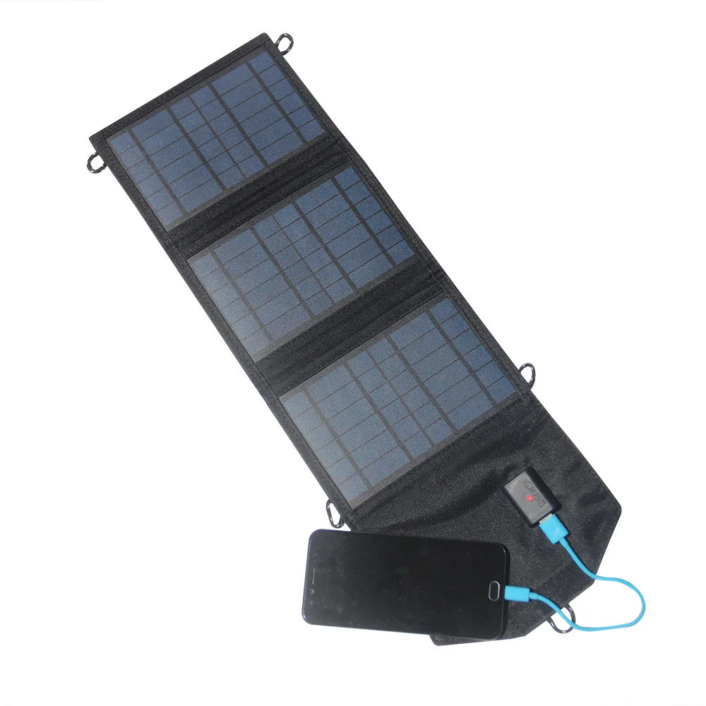 Three-section black foldable USB solar charger opened beside a phone