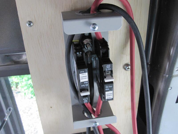 Close-up of two DC circuit breakers (30A and 60A) for a solar PV system, mounted inside a van with red and black wiring.