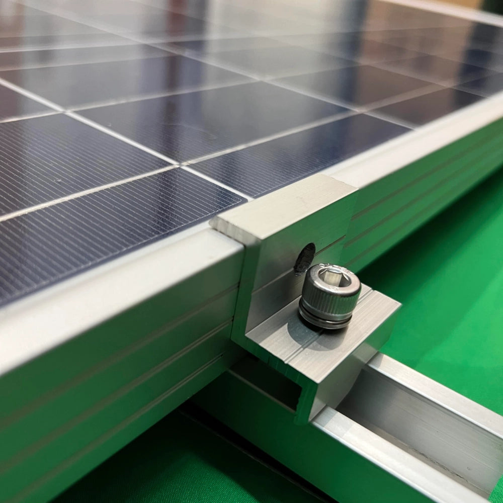 A close-up photograph of an aluminum end clamp securely fastening the edge of a solar panel frame to a mini mounting rail.