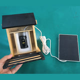 Wooden camera feeder and separate solar panel with connecting cable on a work surface